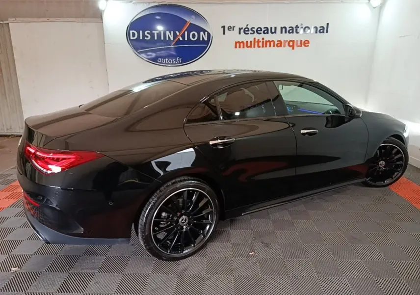 Vue 3/4 arrière droite d'une Mercedes CLA 200 d AMG Line noire avec jantes noires et feux arrière LED allumés.