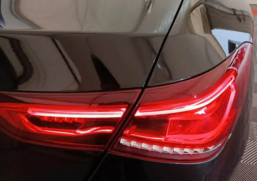 Gros plan sur le feu arrière droit rouge d’une Mercedes CLA 200 d AMG Line noire, finition 2022.