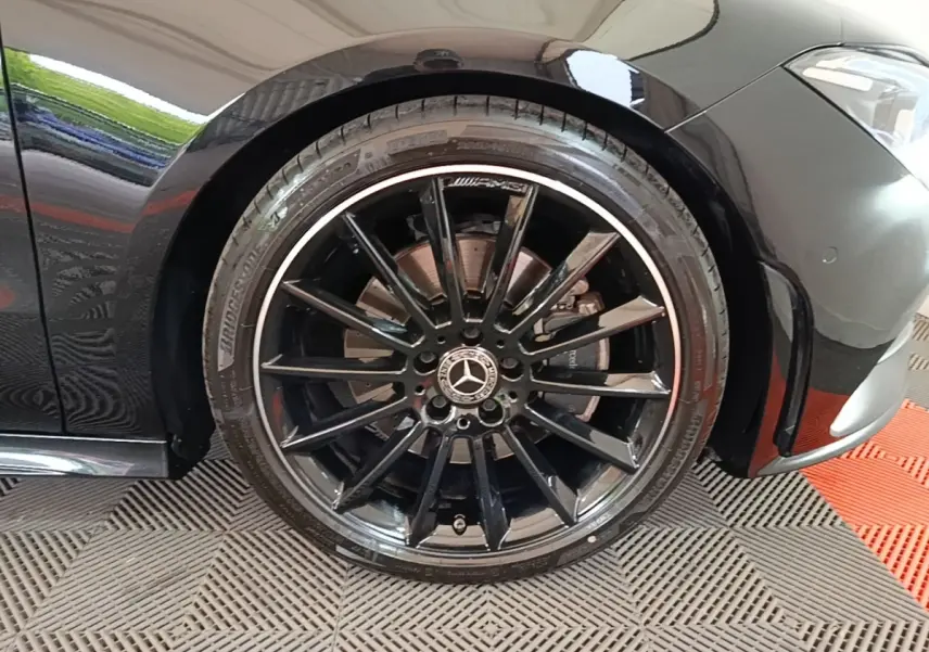 Gros plan sur la roue avant gauche noire AMG avec jante multibranches et logo Mercedes visible sur une Mercedes CLA 200 d AMG Line.