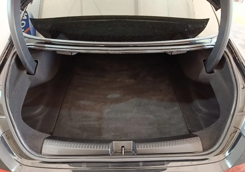 Coffre ouvert vu de l'arrière d'une Mercedes CLA 200 d AMG Line noire, montrant un espace de chargement propre et spacieux.