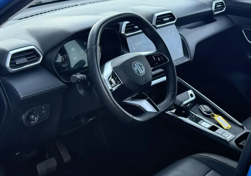 Vue intérieure côté conducteur du MG ZS 1.5 Hybrid+ 197 Luxury 2025, volant cuir noir et écran tactile central.