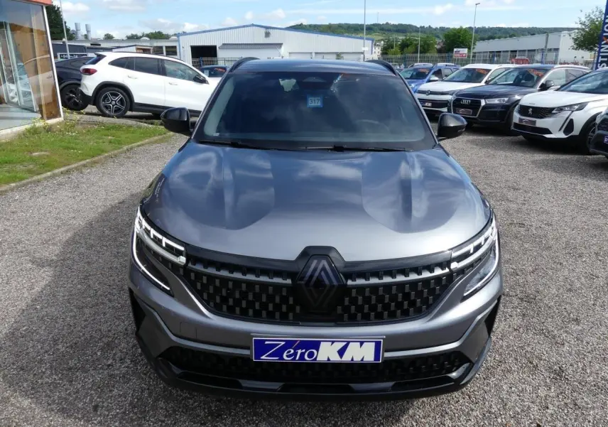 Vue avant d'un Renault Austral gris métallisé avec calandre à damier et logo Alpine noir, en extérieur sur parking.