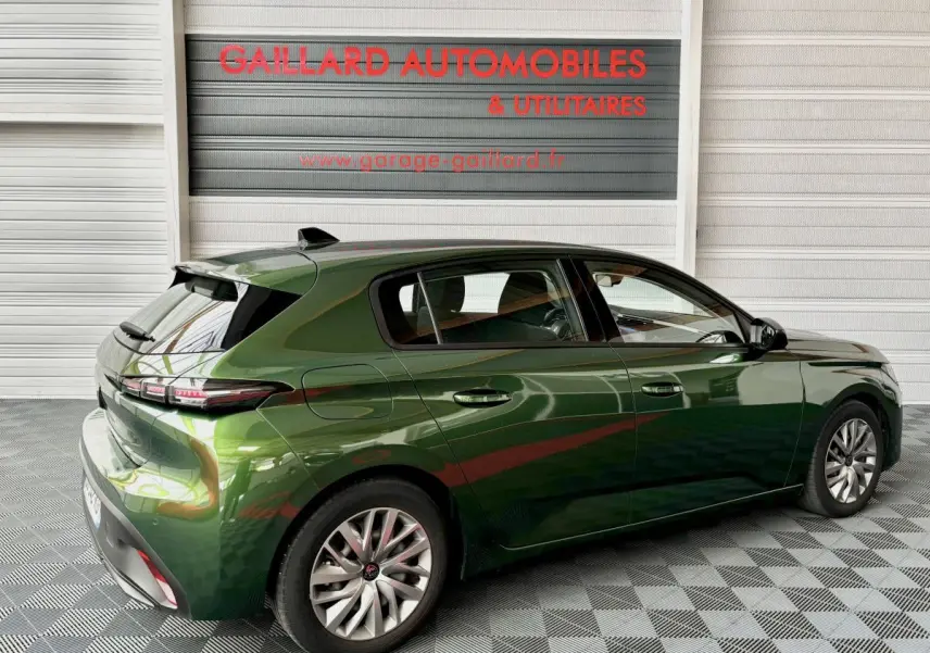 Vue 3/4 arrière droite d'une Peugeot 308 PureTech 110 S&S ACTIVE PACK verte, stationnée en intérieur sur sol damier.