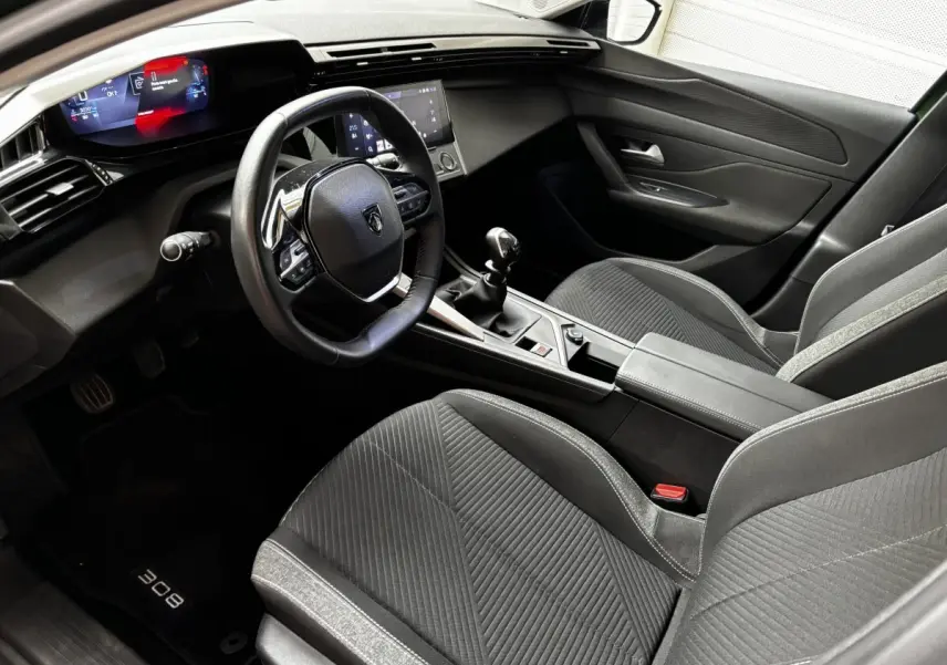 Intérieur avant droit de la Peugeot 308 2022, volant cuir, tableau de bord numérique et sièges tissu noirs.