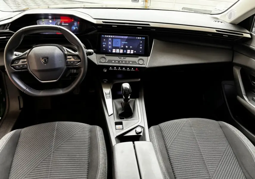 Intérieur de la Peugeot 308 2022 vue de face, volant cuir, écran tactile central et levier de vitesse manuel visibles.