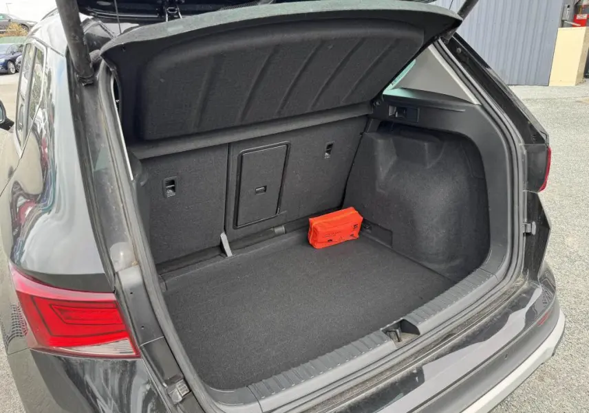 Coffre ouvert côté arrière d'un SEAT Ateca noir 2023, montrant un espace de rangement avec trappe et kit de secours rouge.