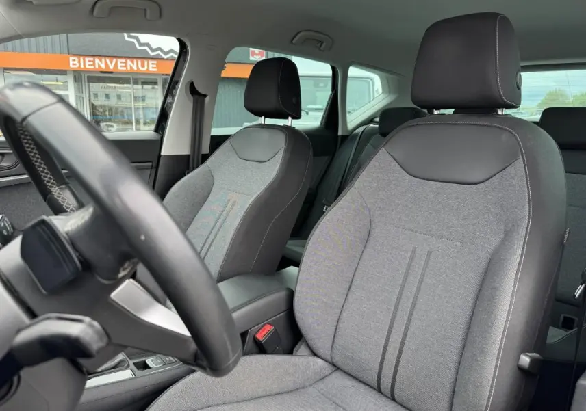 Vue intérieure sur les sièges avant en textile gris et noir du SEAT Ateca 2023, avec volant partiellement visible et arrière-plan extérieur.
