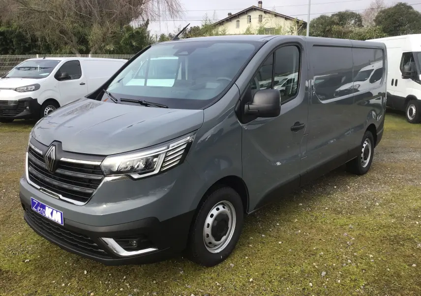 Renault Trafic Fourgon gris urbain en 3/4 avant droit, avec calandre chromée et phares LED distinctifs.
