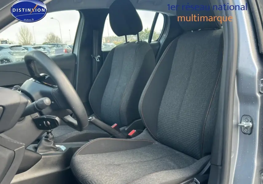 Vue intérieure côté avant droit de la Peugeot 208 1.2 100 Style 2025, sièges tissu gris avec surpiqûres orange.