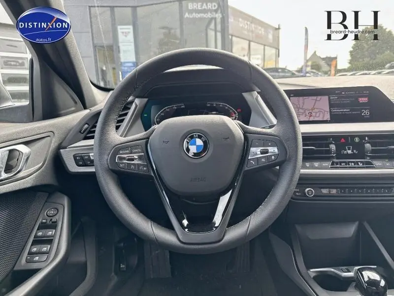 Vue intérieure centrée sur le volant cuir multifonction de la BMW Série 1 116dA, avec tableau de bord numérique et écran tactile.