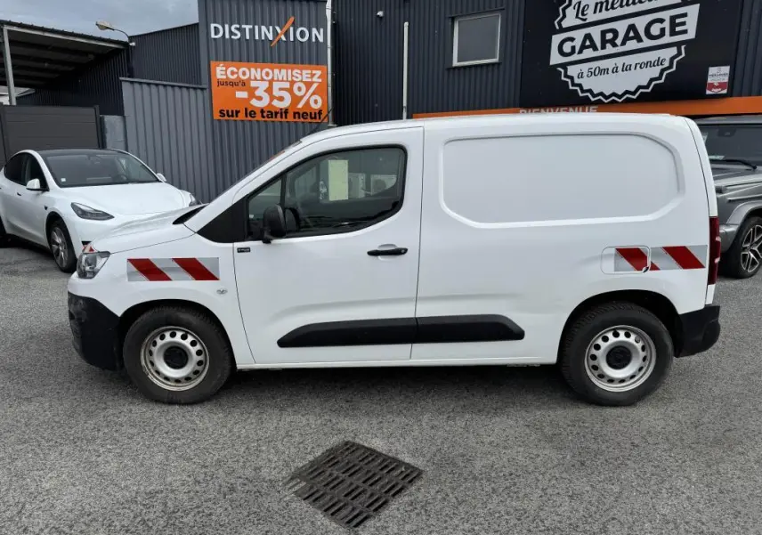Profil côté gauche d'un utilitaire Citroën Berlingo blanc avec bandes réfléchissantes rouges et protections noires.