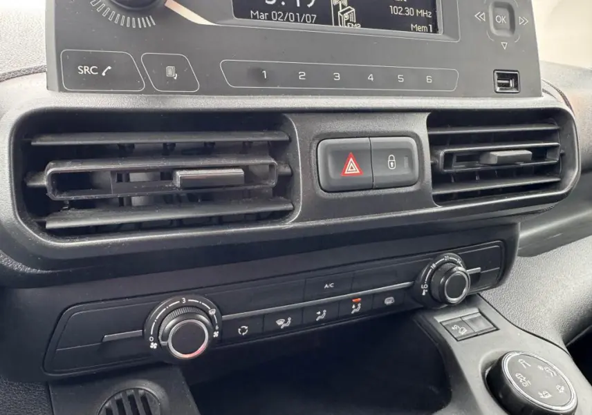Gros plan sur la console centrale noire du Citroën Berlingo blanc, montrant les aérateurs et commandes de climatisation.