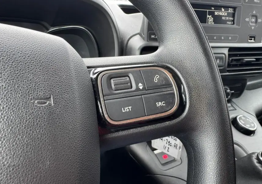 Gros plan sur les commandes au volant noir du Citroën Berlingo 2019, avec tableau de bord et écran radio en arrière-plan.