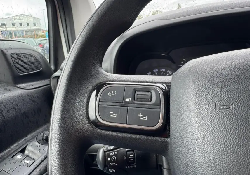 Gros plan sur les commandes au volant noir du Citroën Berlingo blanc, avec vue partielle du tableau de bord et porte côté gauche.