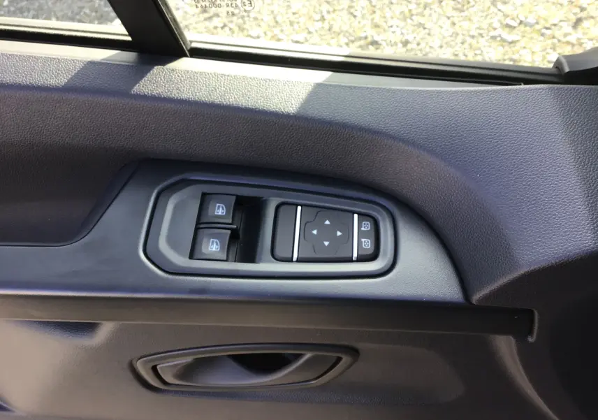 Gros plan sur les commandes de lève-vitres et réglage des rétroviseurs côté gauche du Renault Trafic Fourgon blanc 2025.