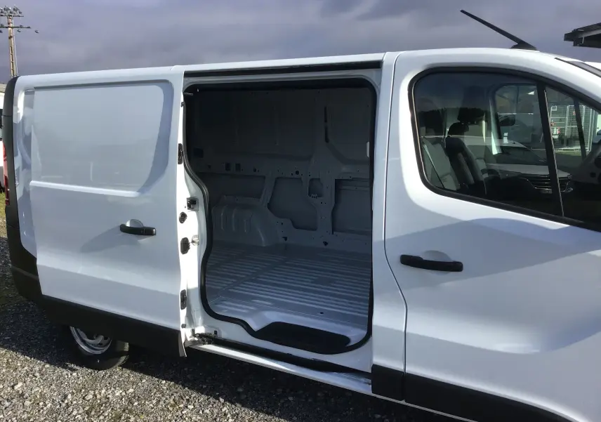 Vue latérale droite d’un Renault Trafic Fourgon blanc 2025 avec porte coulissante ouverte dévoilant l’espace de chargement vide.