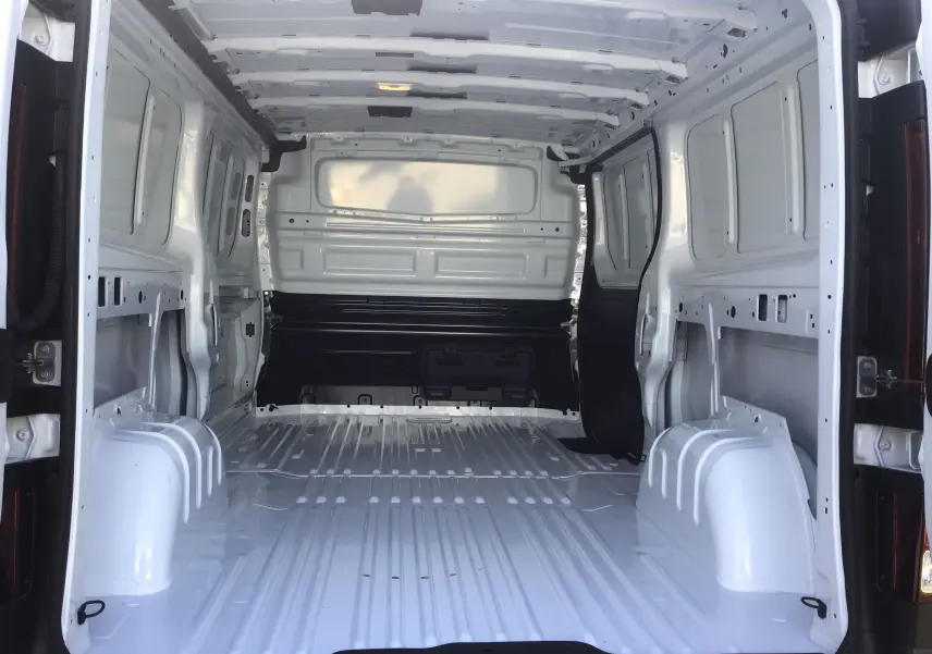 Vue intérieure arrière du fourgon blanc Renault Trafic L2H1 2025, montrant l’espace de chargement vide et métallique.