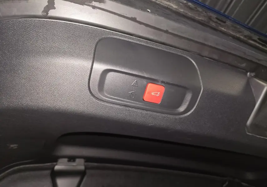 Bouton rouge d'ouverture électrique du hayon sur le panneau intérieur du coffre d'une Peugeot 408 bleu.
