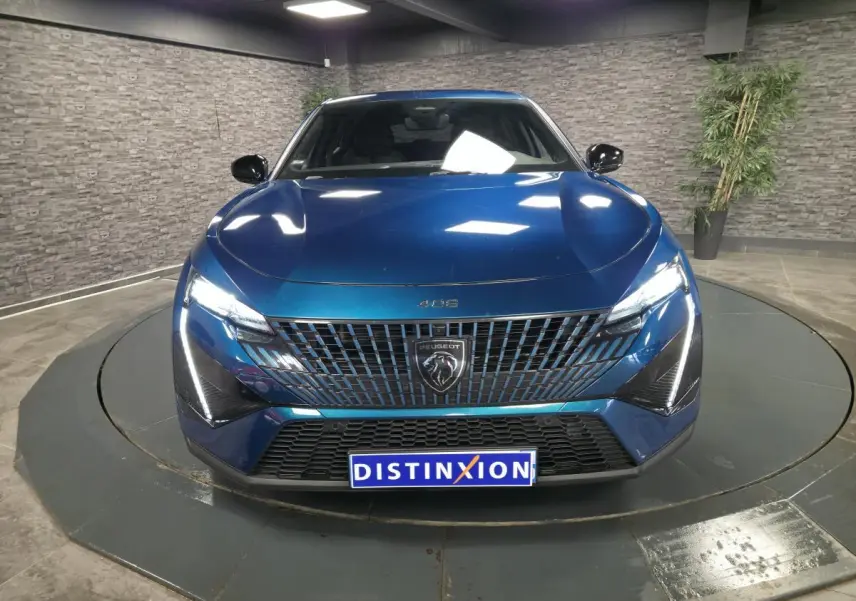 Vue avant d'une Peugeot 408 bleu métallisé avec calandre verticale et feux LED griffés allumés dans un showroom.