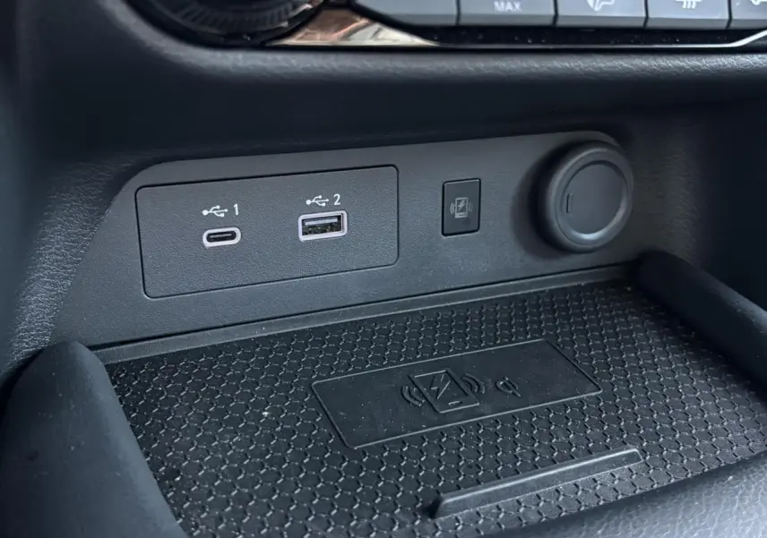 Gros plan sur la console centrale du Nissan Juke 2024, montrant les ports USB, prise 12V et chargeur sans fil.