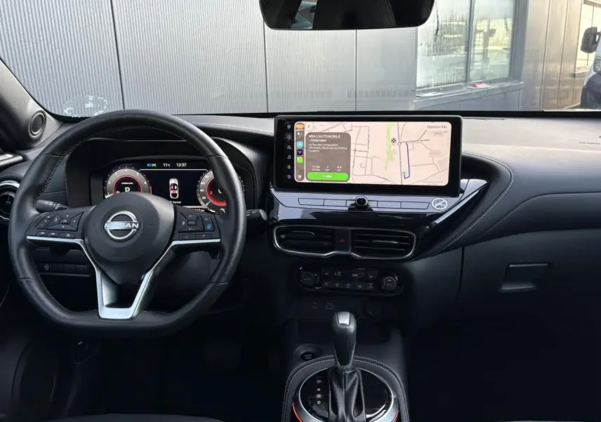 Vue intérieure frontale du Nissan Juke 2024 avec tableau de bord noir, écran tactile central et volant multifonction.