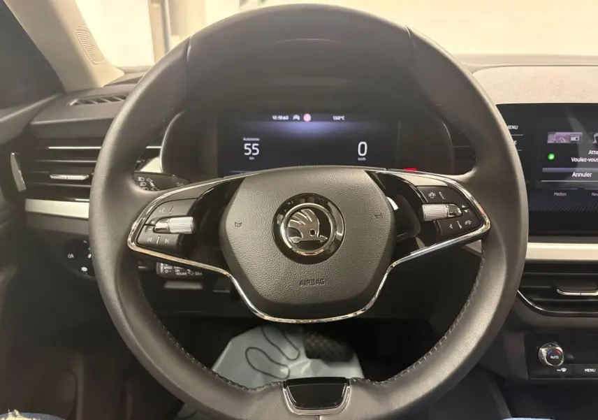 Vue intérieure centrée sur le volant noir de la Skoda Kamiq 2023 avec tableau de bord digital et commandes intégrées.