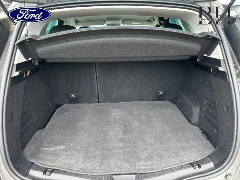 Coffre ouvert vu de l'arrière d'un Renault Scénic gris Cassiopée/Noir Étoilé avec tapis de coffre marqué Scénic.