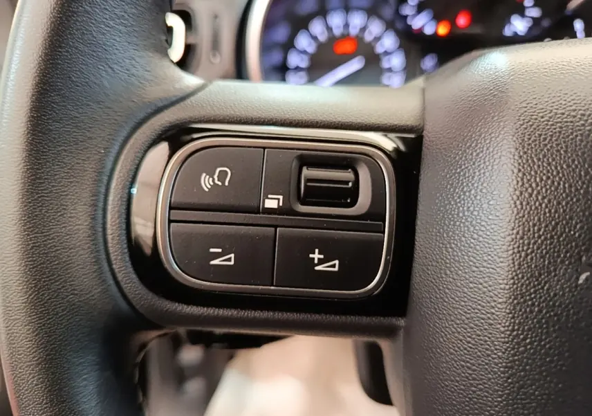Gros plan sur les commandes du volant cuir noir de la Citroën C3 2022, avec tableau de bord flou en arrière-plan.