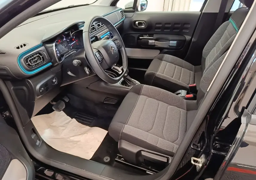 Vue intérieure côté conducteur de la Citroën C3 noire 2022, avec tableau de bord et sièges gris détaillés.
