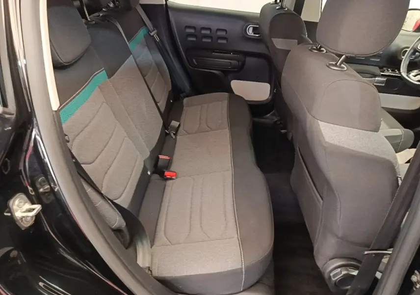 Vue intérieure côté arrière gauche de la Citroën C3 noire 2022, montrant la banquette arrière en tissu gris avec bande verte.