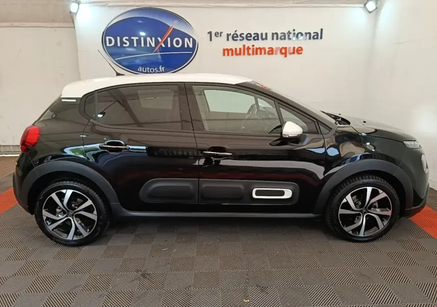 Vue de profil droit d'une Citroën C3 noire avec toit blanc et jantes alliage bicolores dans un showroom.
