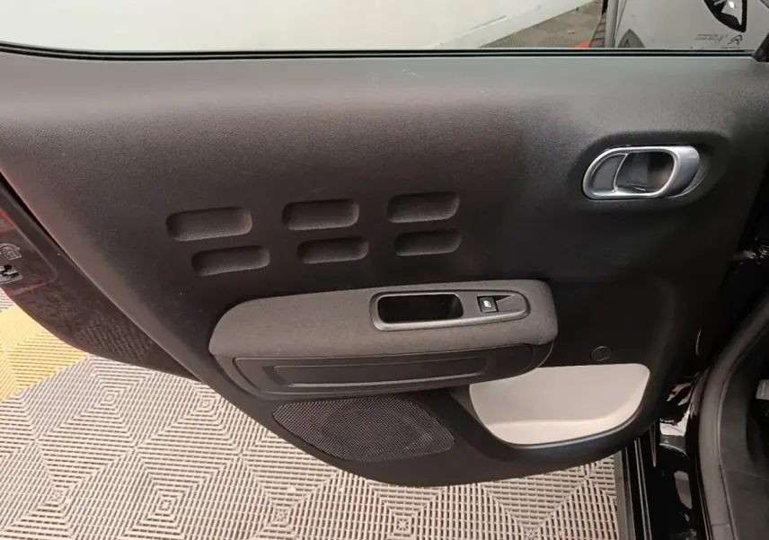 Vue rapprochée de la porte intérieure côté gauche noire de la Citroën C3 avec poignée argentée et bouton de vitre électrique.