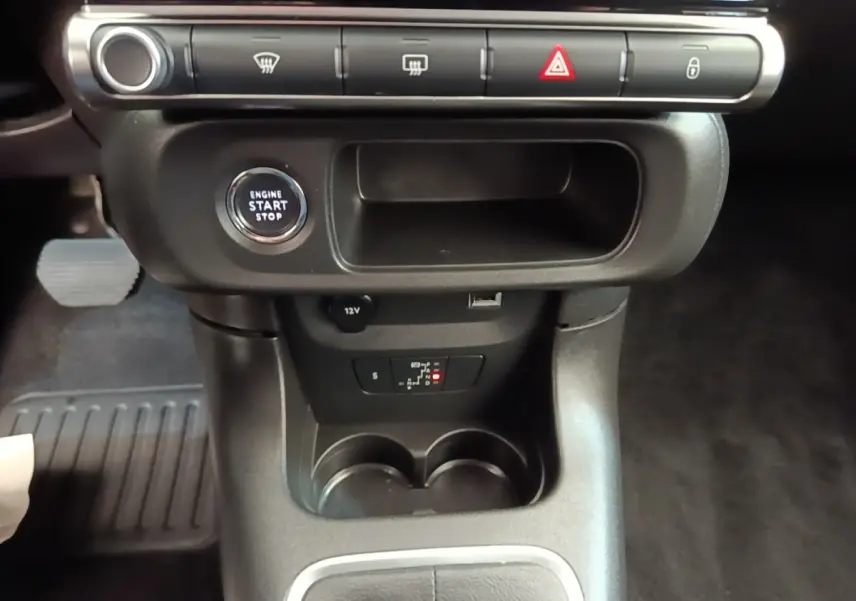 Gros plan intérieur sur la console centrale noire de la Citroën C3, avec bouton start/stop et prises 12V et USB visibles.