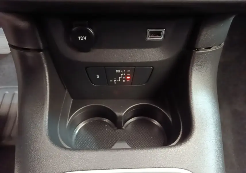 Gros plan sur la console centrale noire de la Citroën C3, avec porte-gobelets, prise 12V et indicateur de boîte auto éclairé.