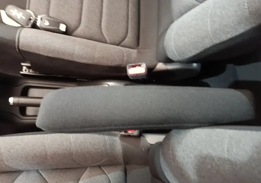 Vue plongeante sur l'accoudoir central et sièges avant en tissu gris foncé de la Citroën C3 noire.