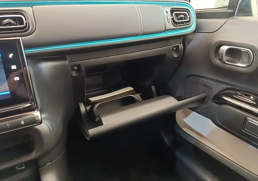 Intérieur de la Citroën C3 2022, vue côté passager sur la boîte à gants ouverte et tableau de bord noir avec liseré bleu.