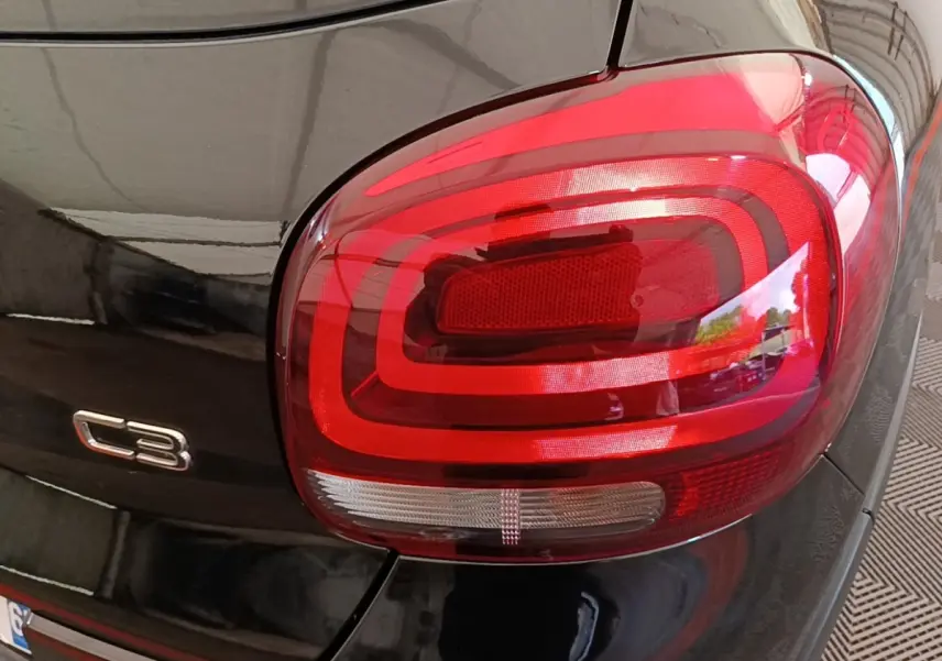 Gros plan sur le feu arrière droit rouge et le logo C3 d'une Citroën C3 noire vue de l'arrière.