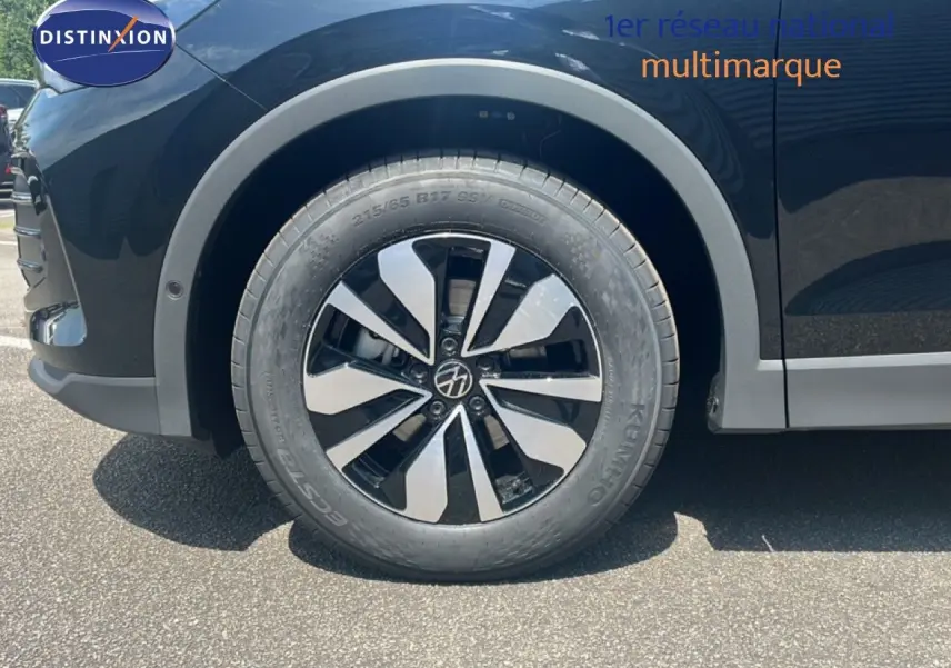 Gros plan sur la roue avant gauche du Volkswagen Tiguan noir grenadilla métallisé, mettant en valeur la jante design bicolore.