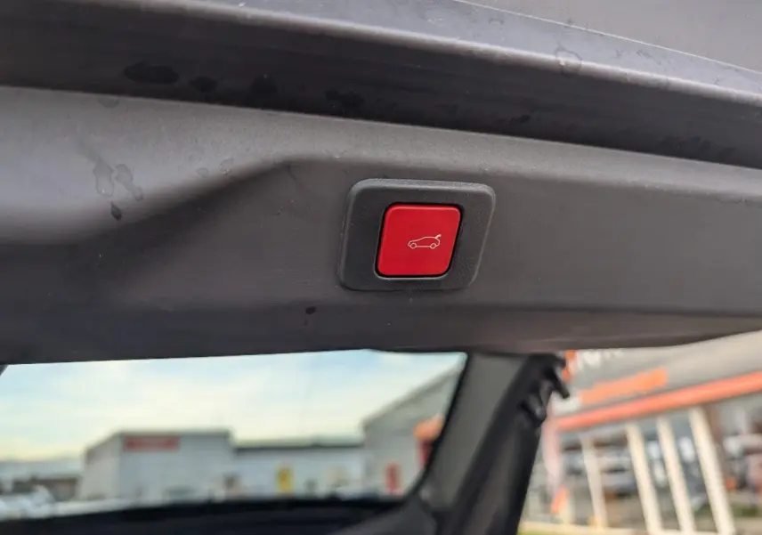 Bouton rouge d'ouverture électrique du hayon visible depuis l'intérieur arrière d'un Peugeot 3008 blanc.