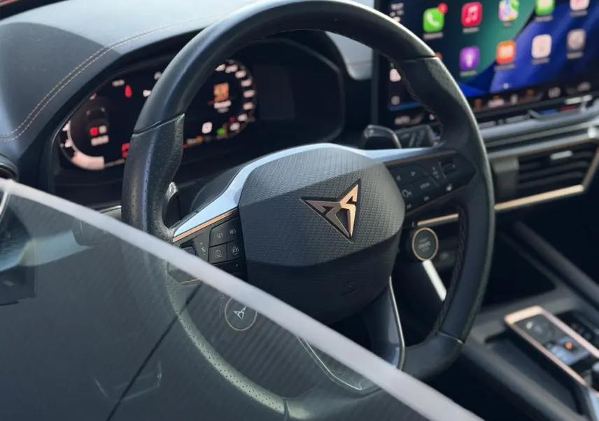 Vue rapprochée du volant cuir noir perforé avec logo CUPRA, tableau de bord digital et écran tactile lumineux.