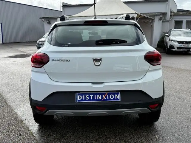 Vue arrière d'une Dacia Sandero Stepway blanche 2021 avec toit équipé de barres de toit et plaque Distinxion.