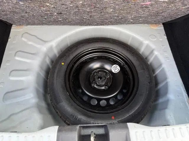 Pneu de secours noir avec étiquette 80 km/h dans le coffre d'une Dacia Sandero Stepway blanche, vue de dessus.