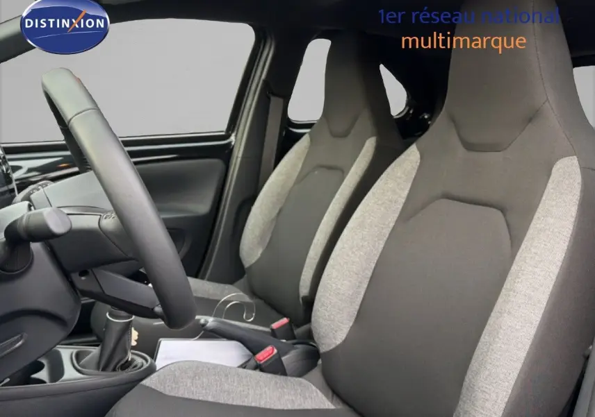 Vue intérieure côté conducteur montrant les sièges avant bi-ton gris et noir de la Toyota Aygo X 2025.