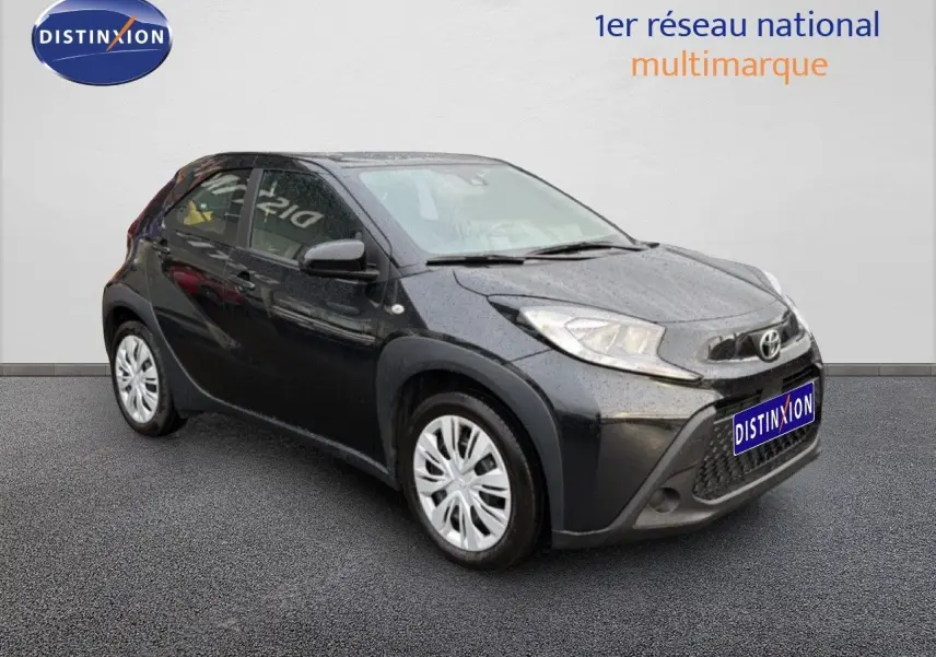 Toyota Aygo X noir vue 3/4 avant droit avec calandre distinctive et jantes argentées sur sol gris.