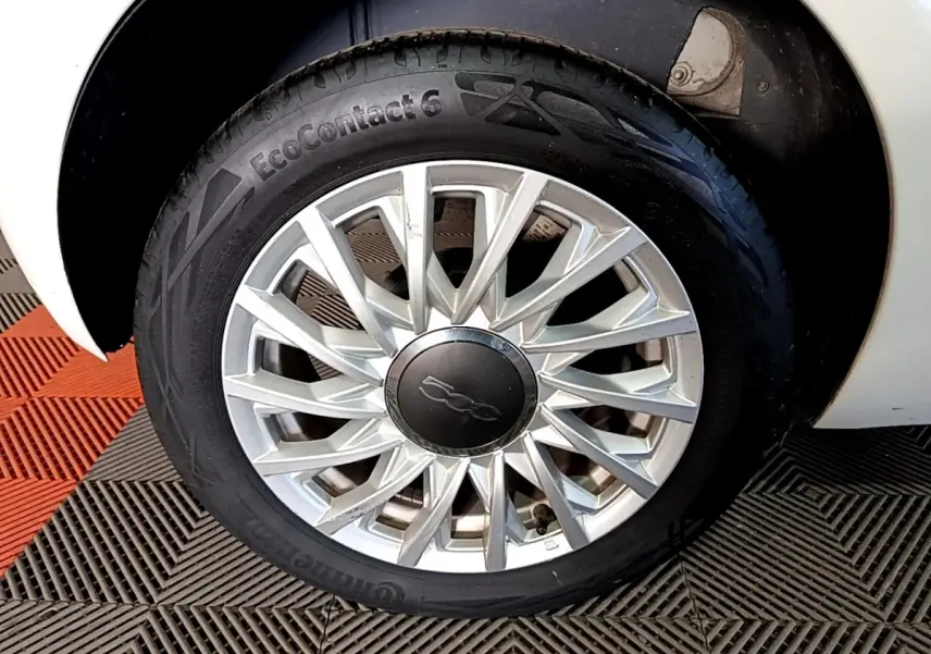 Gros plan sur la roue avant droite d'une FIAT 500 blanche avec jante alliage au design étoilé.