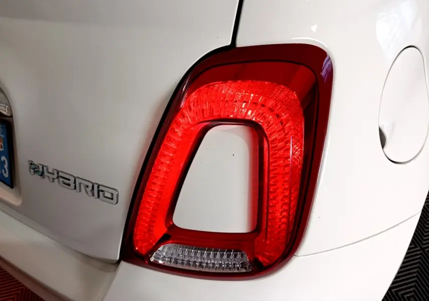 Gros plan sur le feu arrière droit rouge et blanc d'une FIAT 500 Hybrid blanche, avec le logo Hybrid visible sur l'aile arrière.