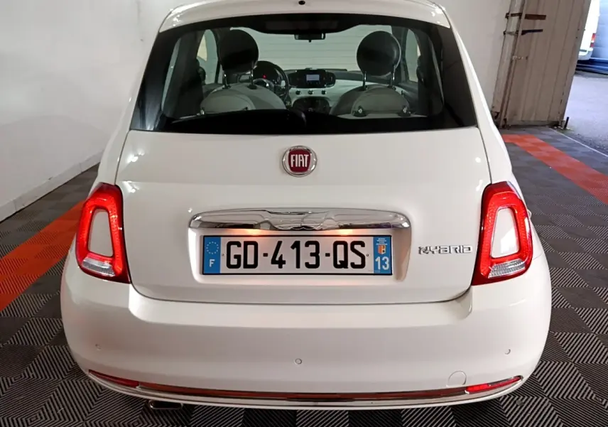 Vue arrière d'une FIAT 500 blanche hybride, avec feux arrière allumés et logo "Hybrid" visible à droite.