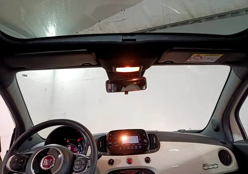 Vue intérieure avant de la Fiat 500 Hybrid blanche, avec tableau de bord brillant et écran tactile central allumé.