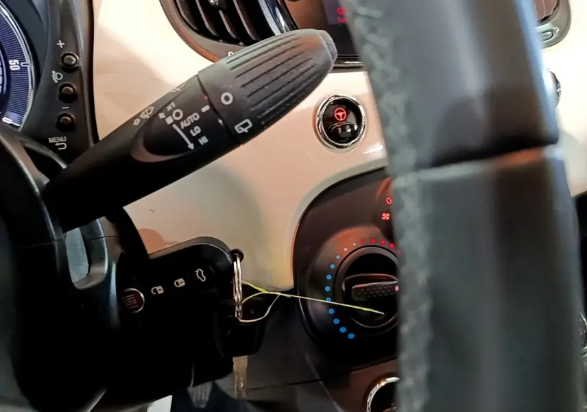 Gros plan sur le tableau de bord blanc et le volant noir de la Fiat 500 Hybrid, avec commandes et clé insérée.