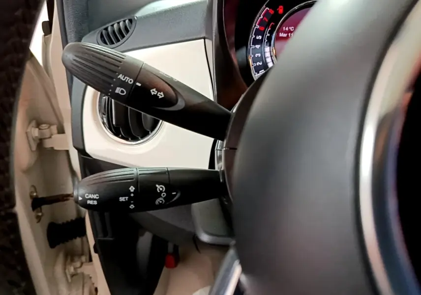 Gros plan sur la colonne de direction et les commandes au volant d’une Fiat 500 blanche, tableau de bord partiellement visible.